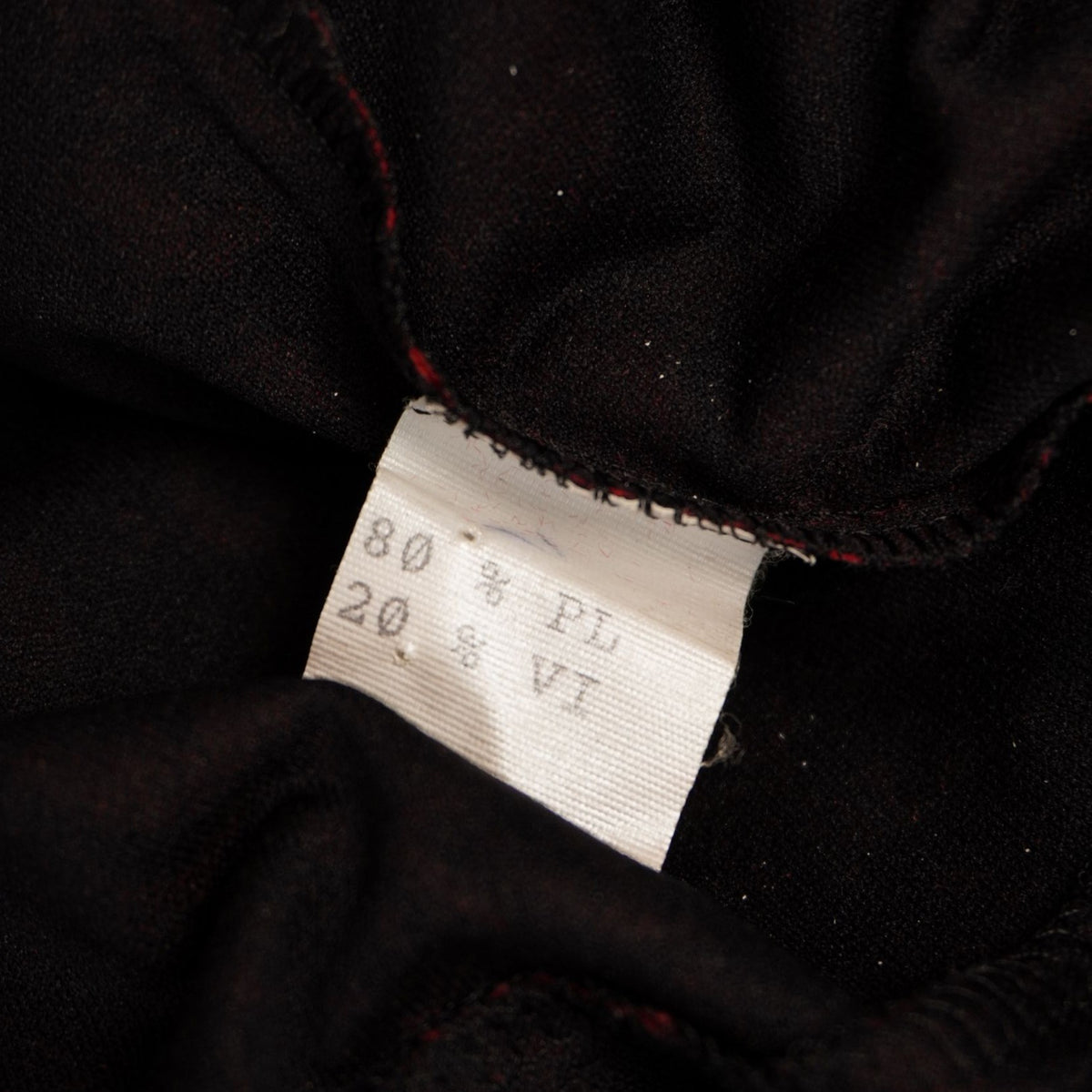 Dettaglio dell'etichetta tecnica interna che indica la composizione 80% poliestere e 20% viscosa della blusa.