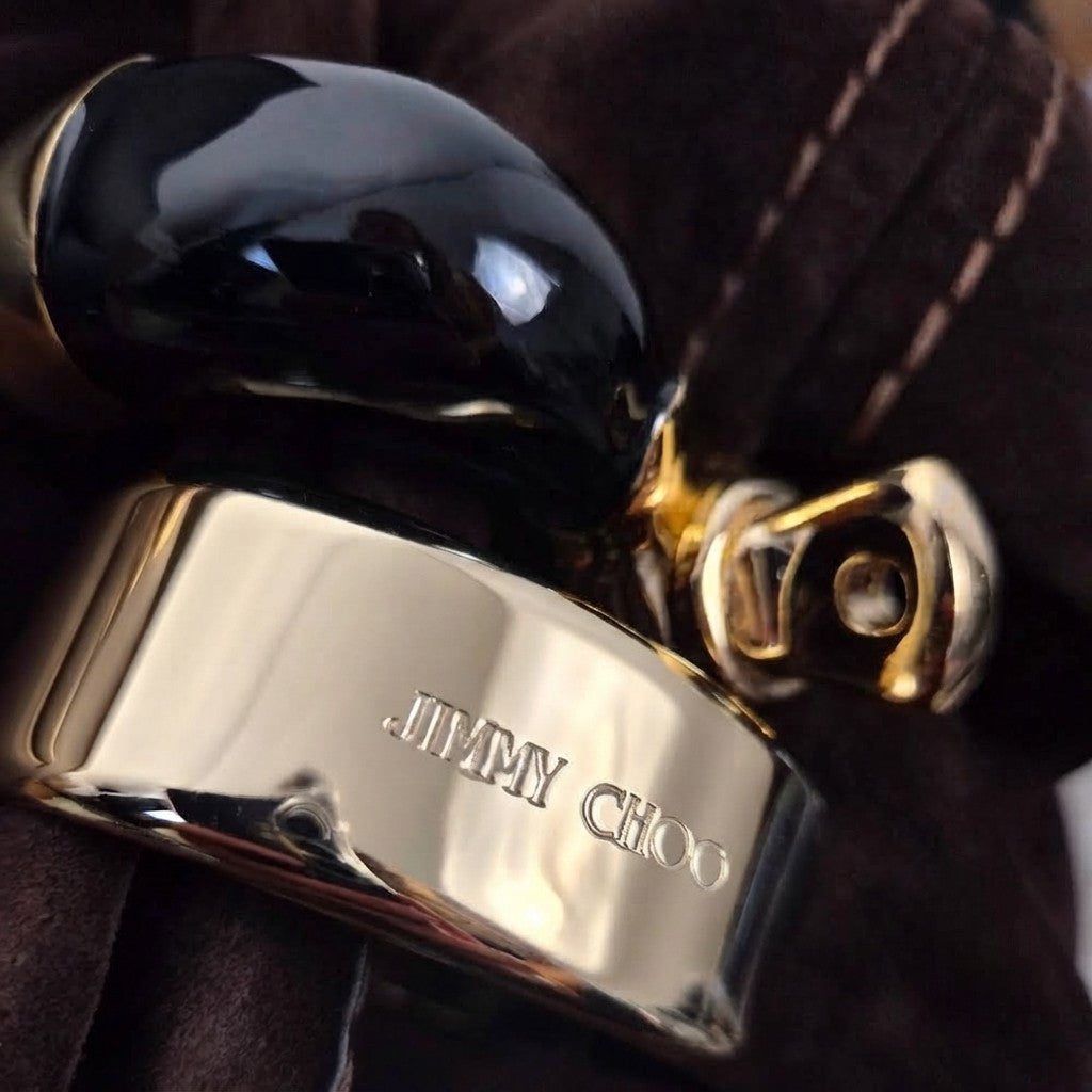  Primo piano dell'incisione del logo Jimmy Choo sul bracciale metallico rigido dorato lucido.