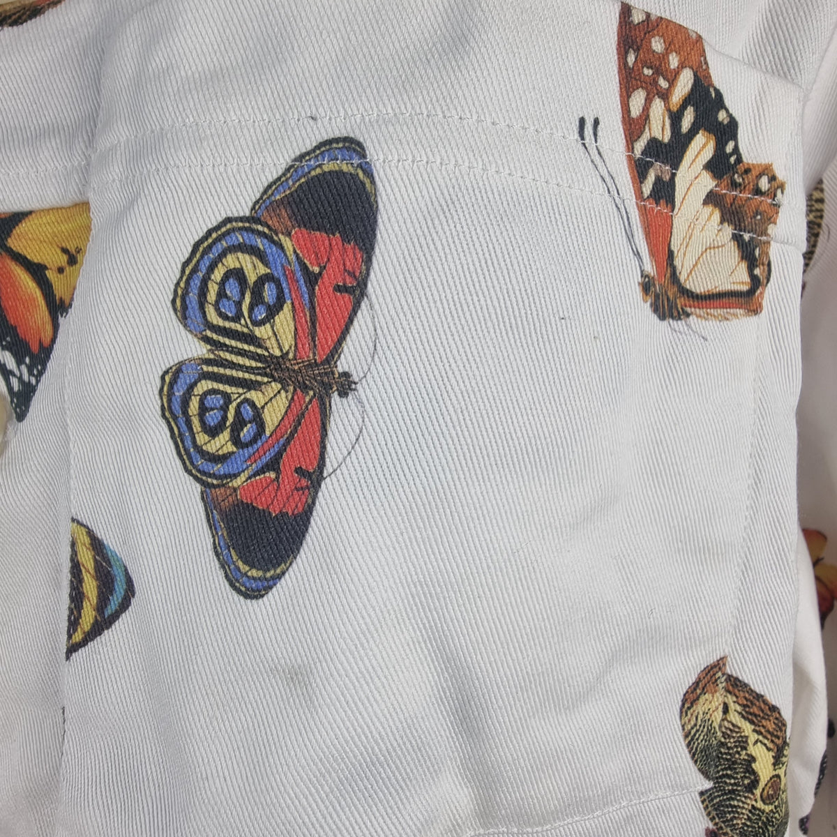 Primo piano del taschino frontale della giacca con stampe di farfalle colorate.