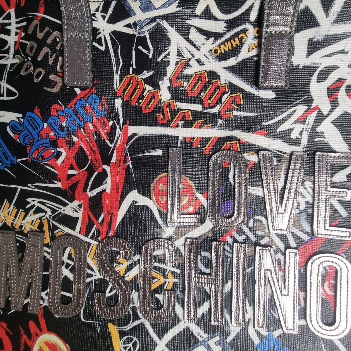 Primo piano del testo Love Moschino applicato in rilievo sulla superficie stampata a graffiti.