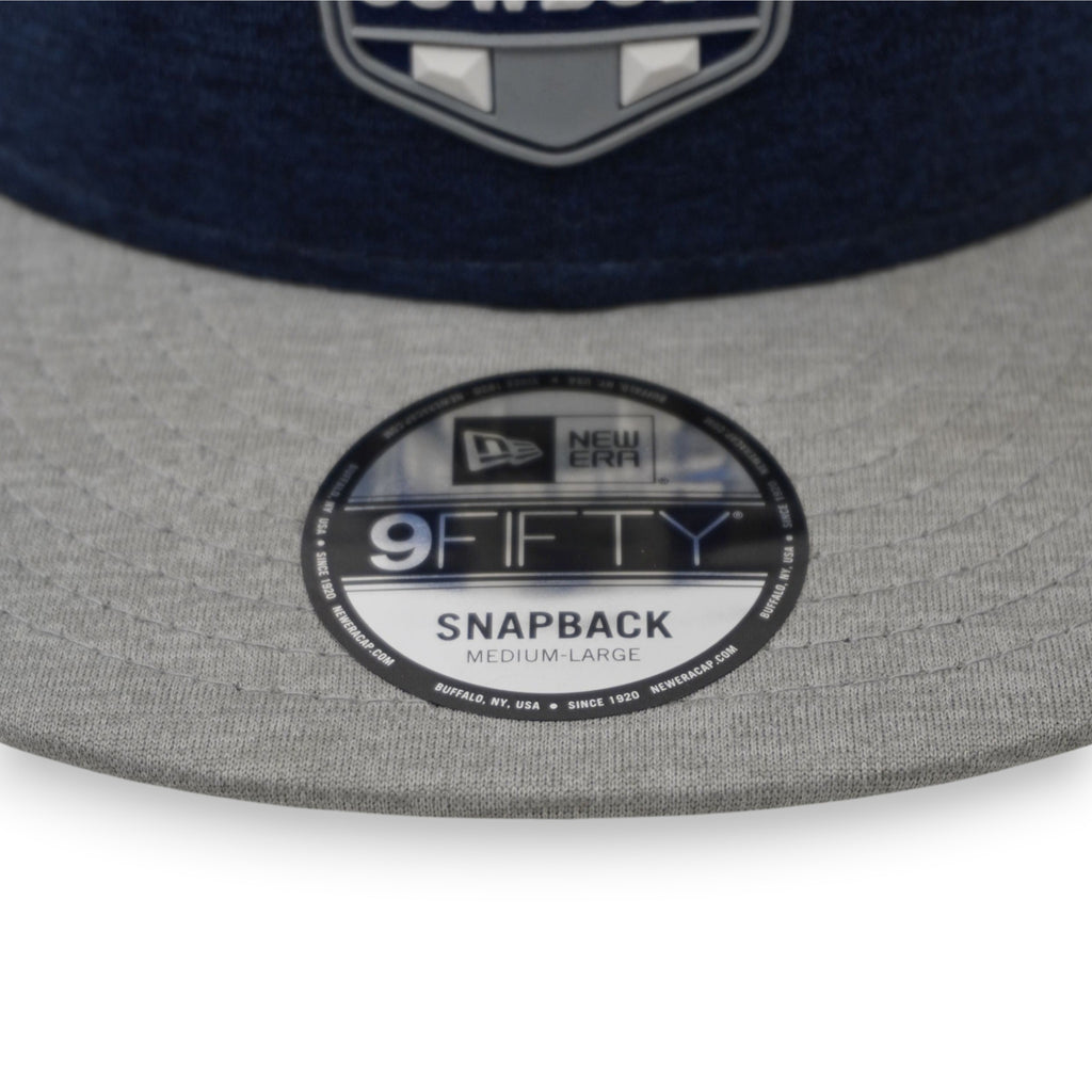 Primo piano dello sticker circolare lucido originale New Era 9FIFTY Snapback Medium-Large sulla visiera grigia.