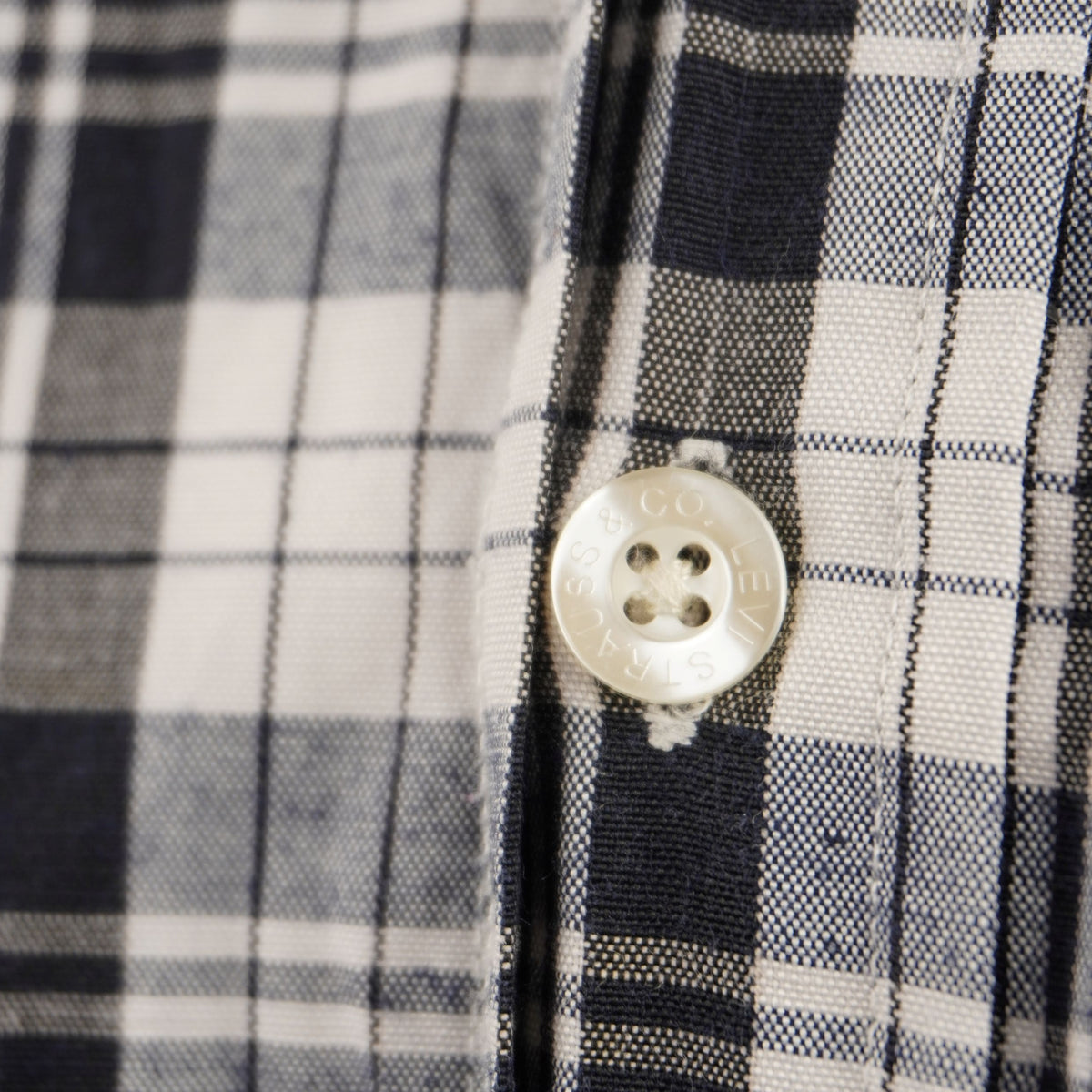 Dettaglio ravvicinato di un bottone bianco perlato cucito sulla patta frontale di una camicia vintage Levi's in cotone a scacchi.