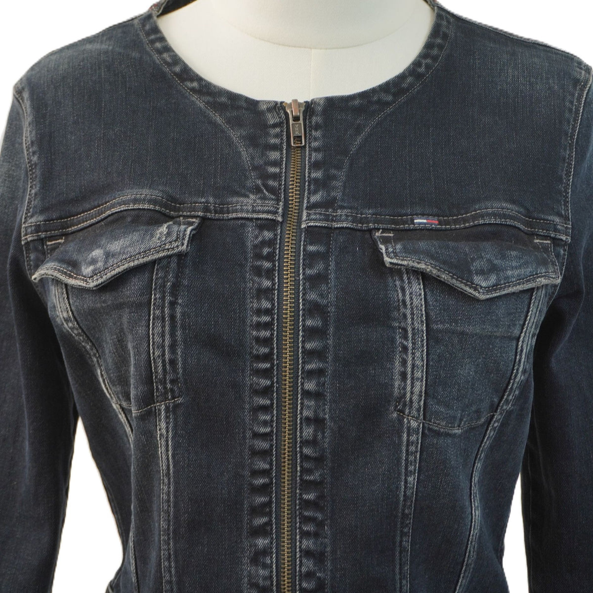 Primo piano del busto della giacca in denim scuro sul manichino, con focus sulle pattine delle tasche pettorali e sui dettagli delle cuciture verticali.
