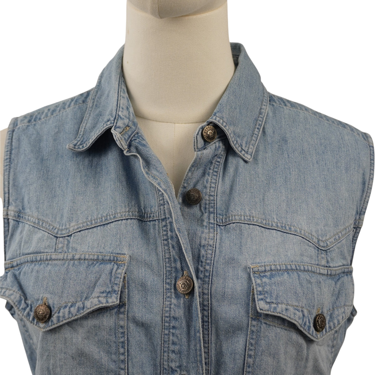 Primo piano del colletto classico a camicia e dei taschini anteriori del gilet Versace Jeans Couture con bottoni metallici logati.