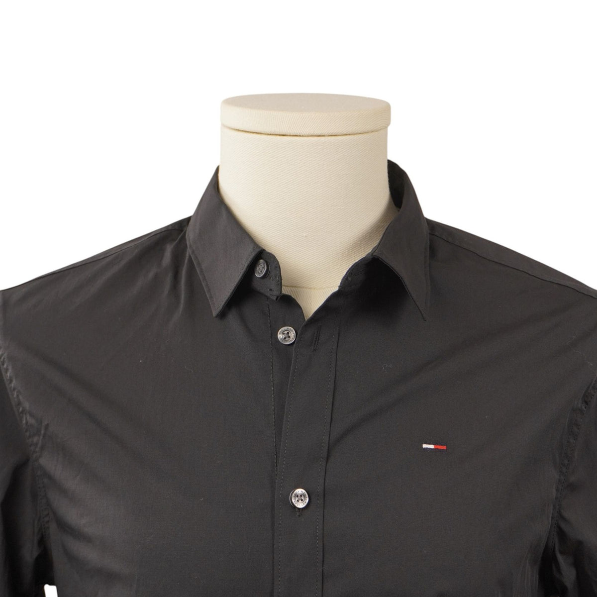 Primo piano frontale del colletto stile Kent e della parte superiore del busto della camicia abbottonata su manichino chiaro.