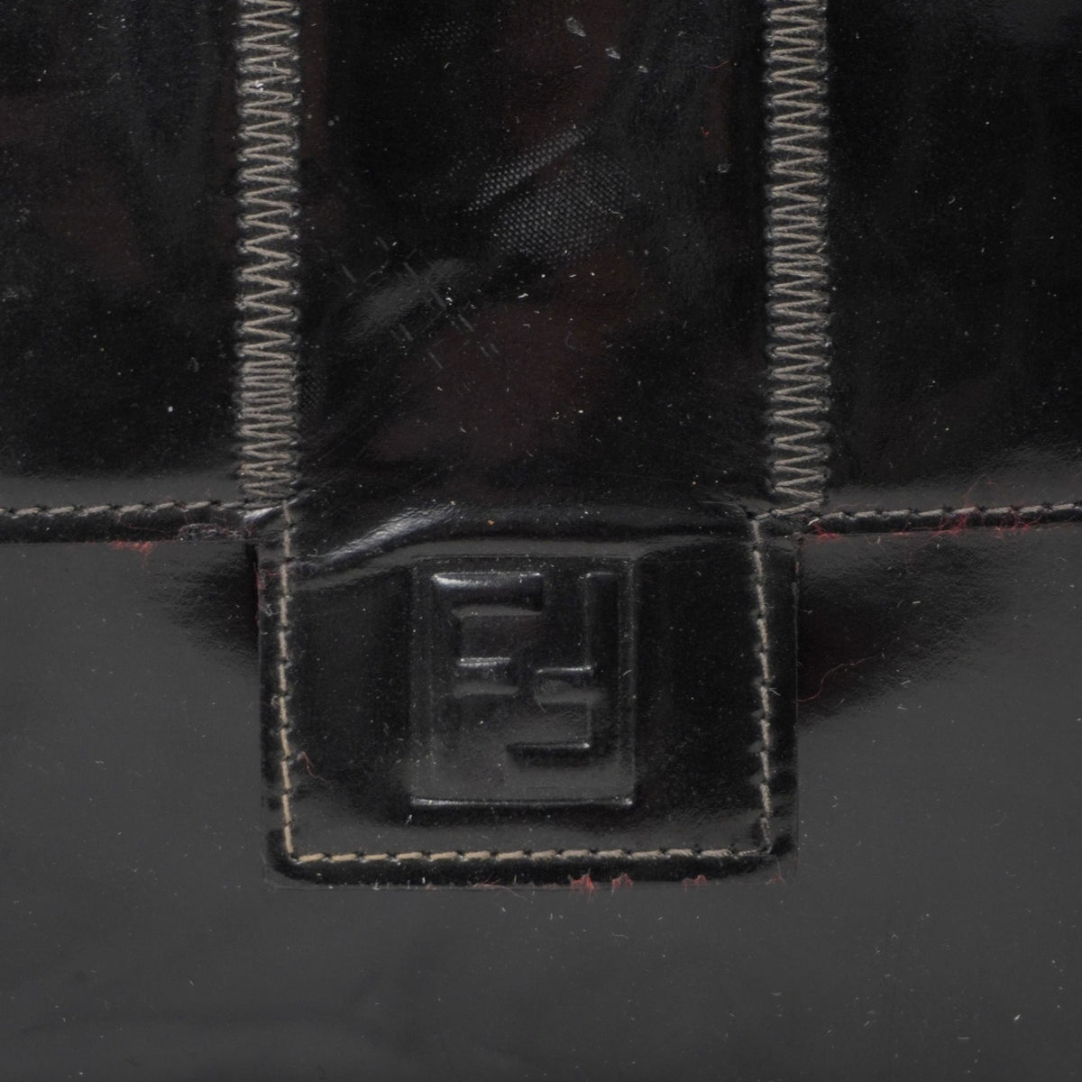 Primo piano del logo iconico FF di Fendi impresso a rilievo sulla patta frontale della borsa in pelle lucida.
