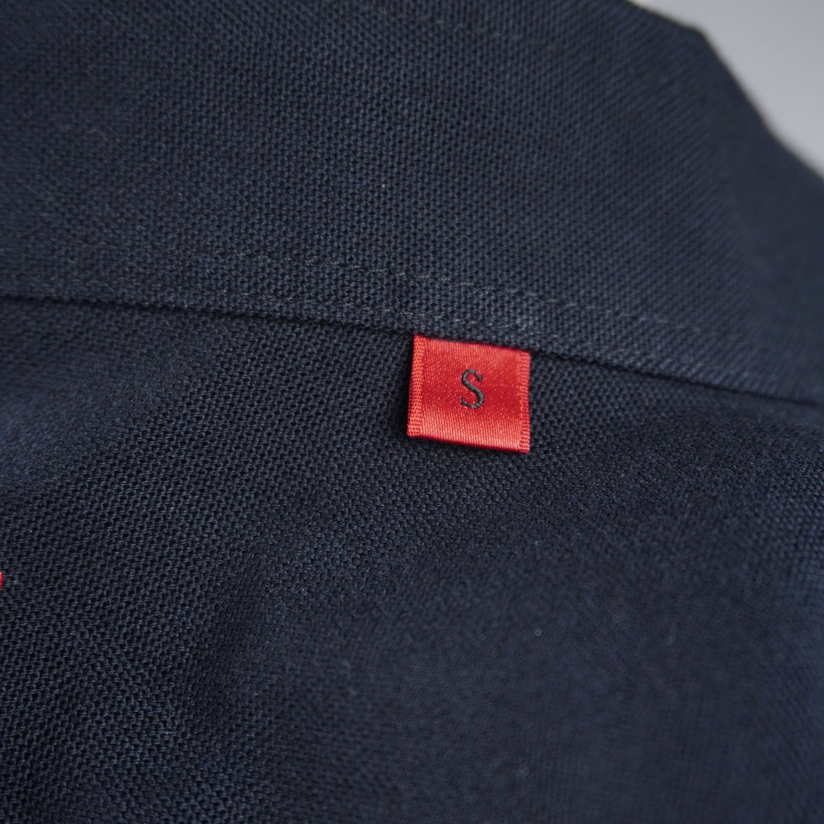 Dettaglio della piccola etichetta rossa con logo HUGO cucita sulla cucitura laterale della camicia nera.