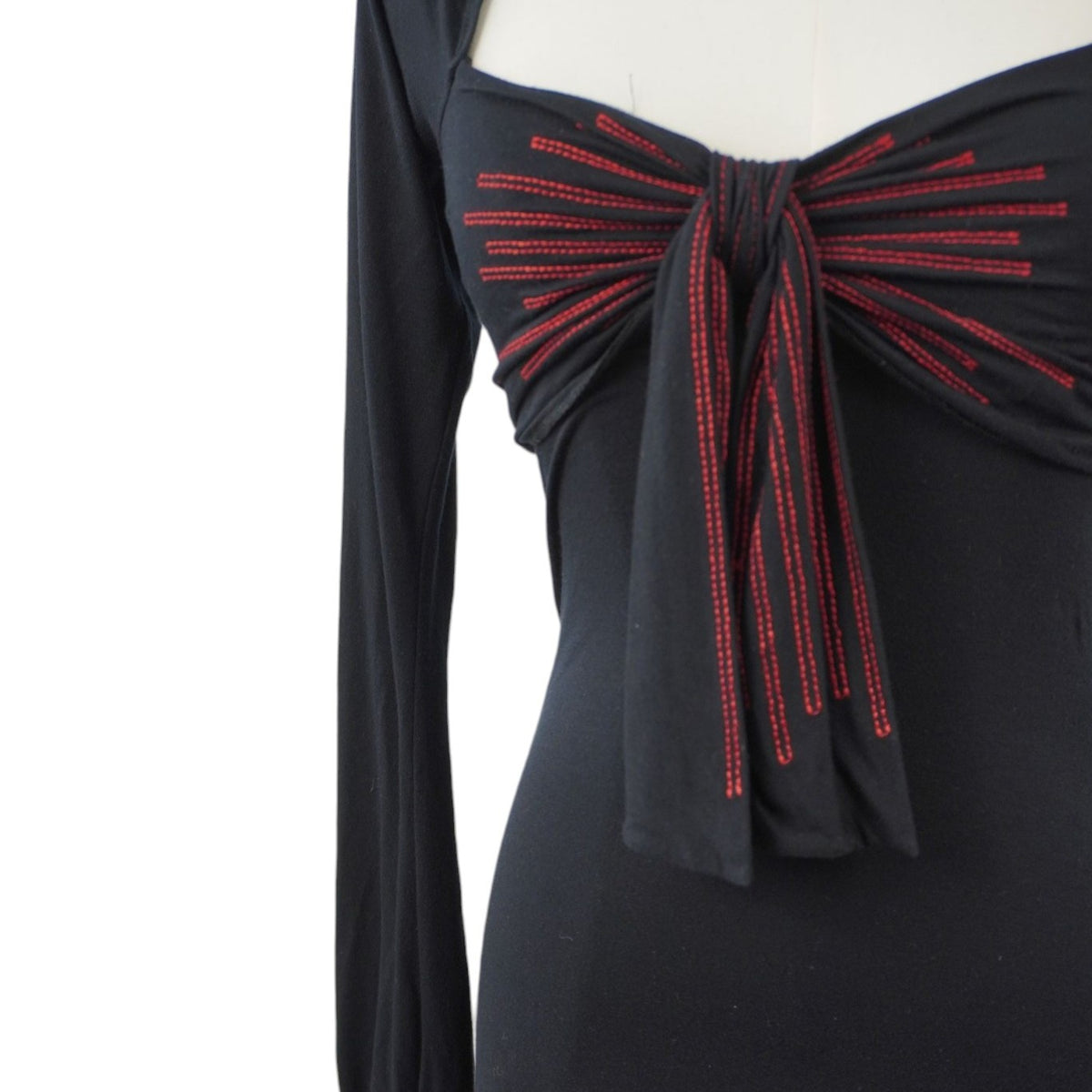  Inquadratura ravvicinata del maxi fiocco sul décolleté con righe verticali ricamate in filo rosso acceso a contrasto.