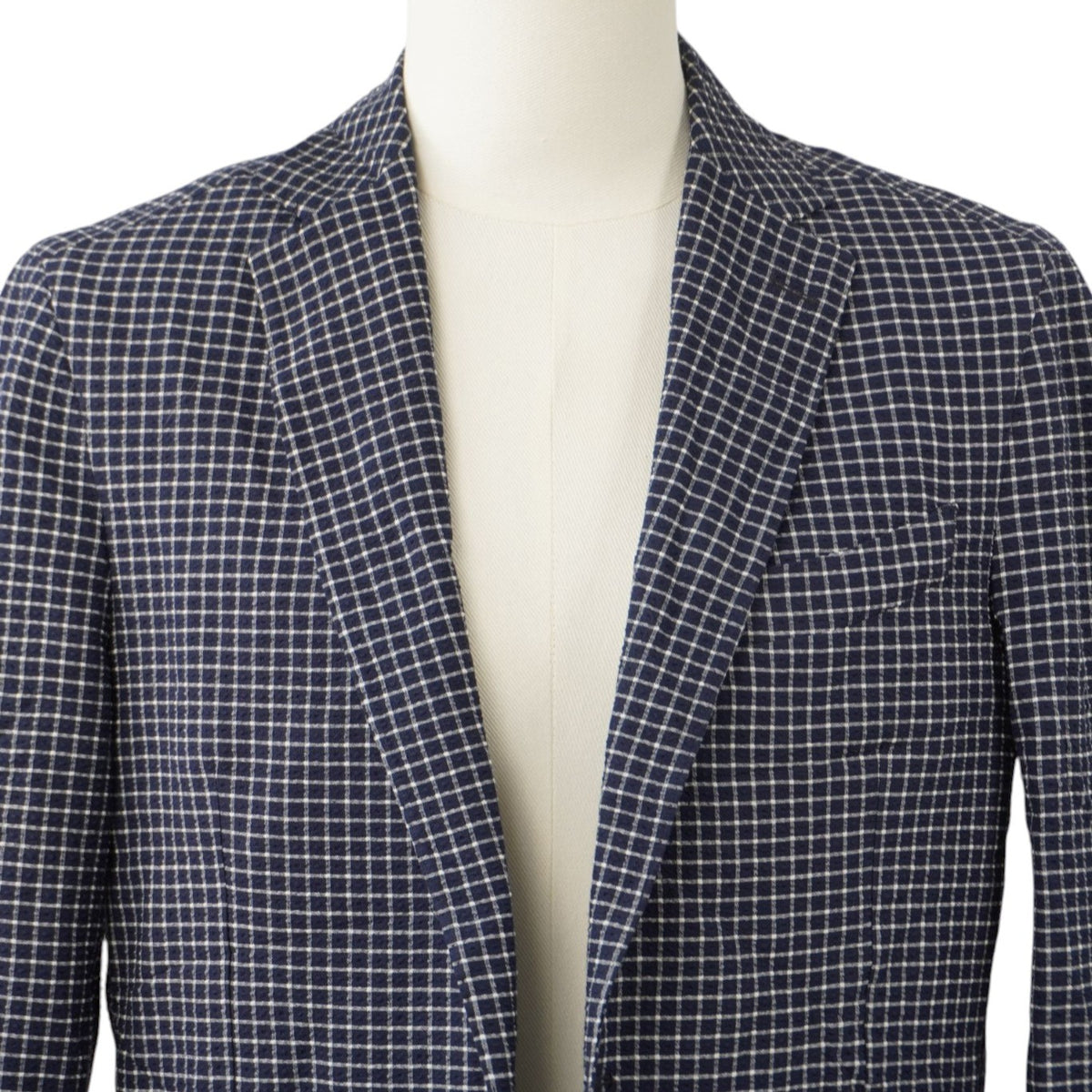Primo piano frontale del colletto e dei revers a lancia della giacca sartoriale a quadretti blu navy e bianchi.