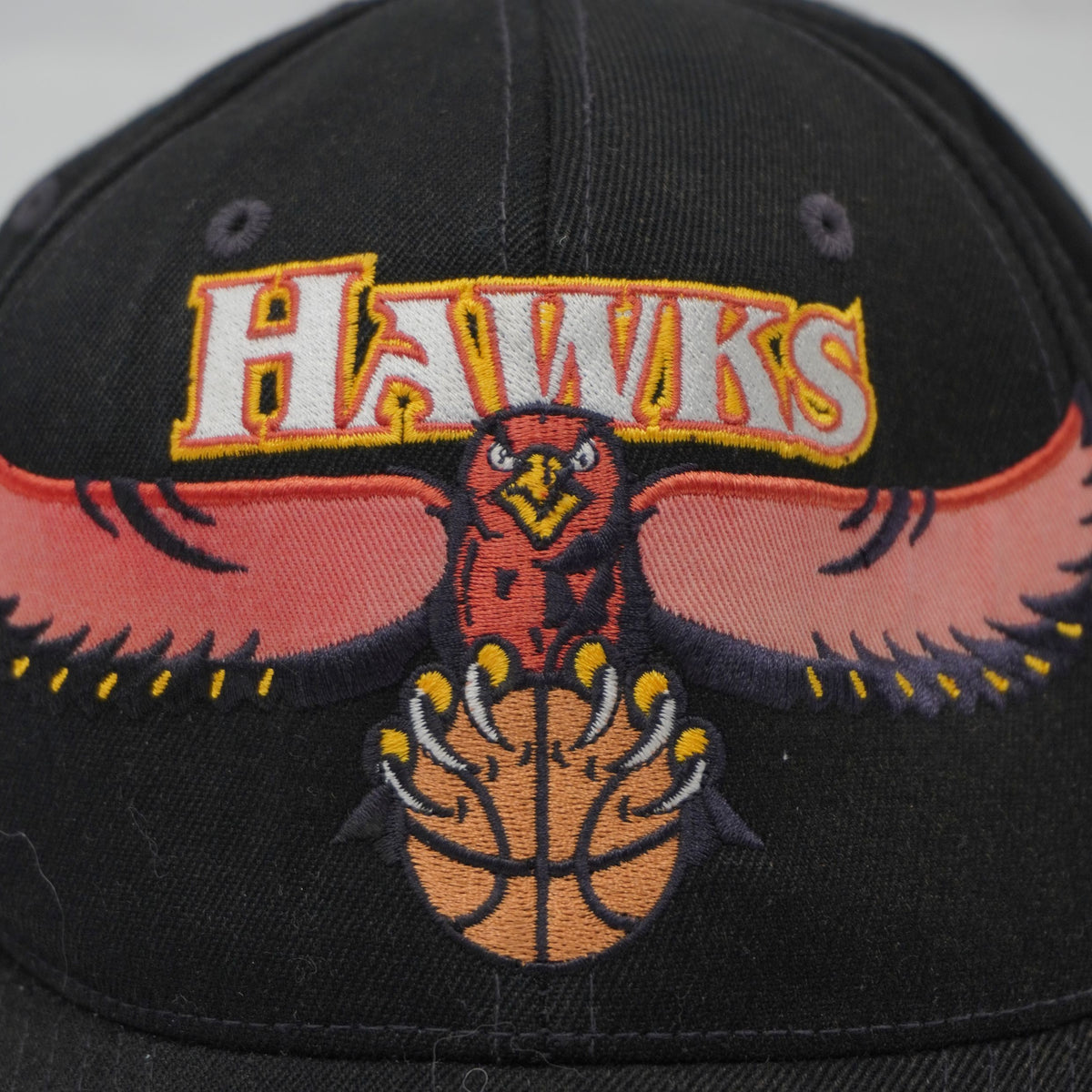 primo piano del ricamo ad alta densità del logo Atlanta Hawks con aquila e palla da basket su corona nera.