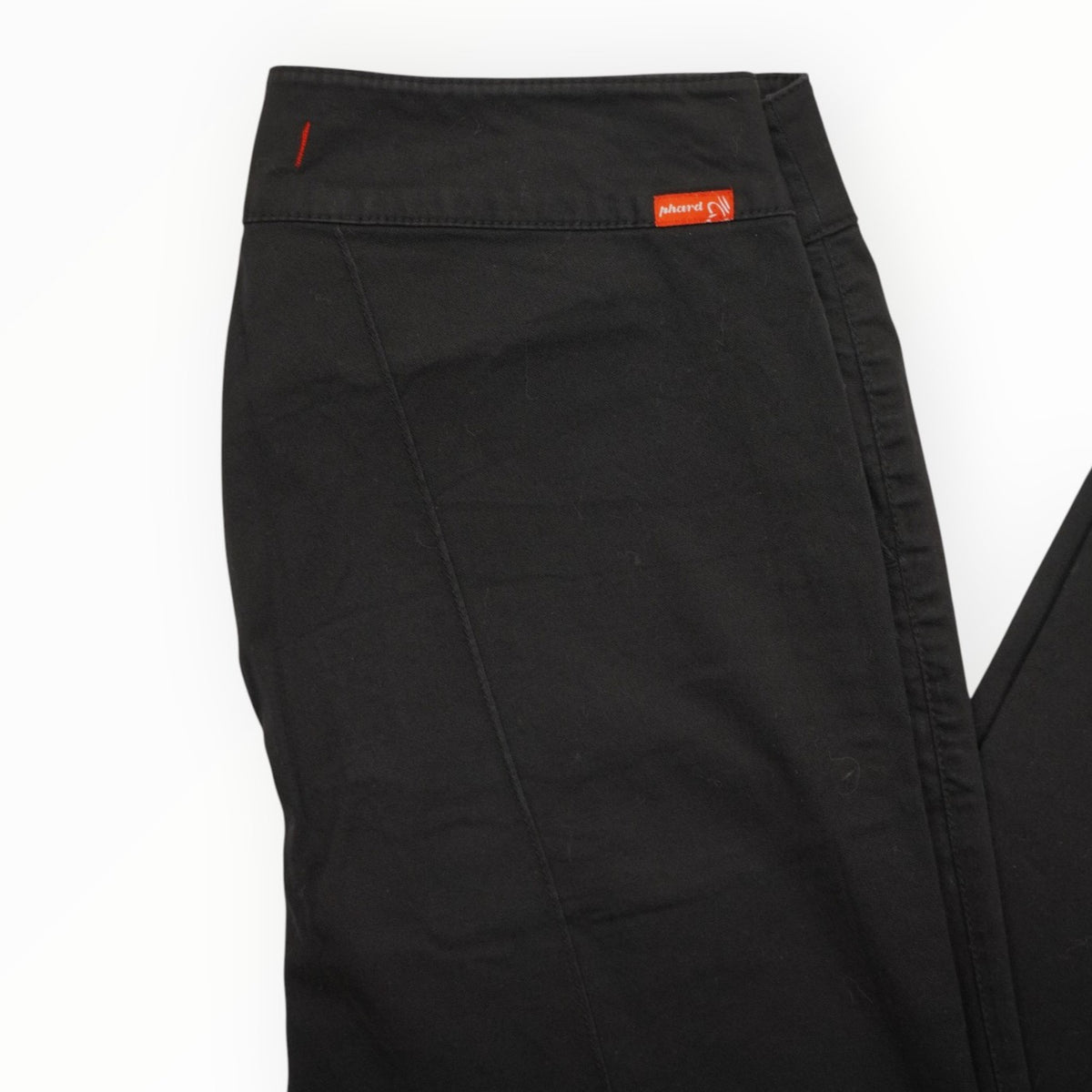  Dettaglio ravvicinato della vita medio-bassa dei pantaloni neri con il caratteristico tag arancione del brand Phard Jeans sul retro.