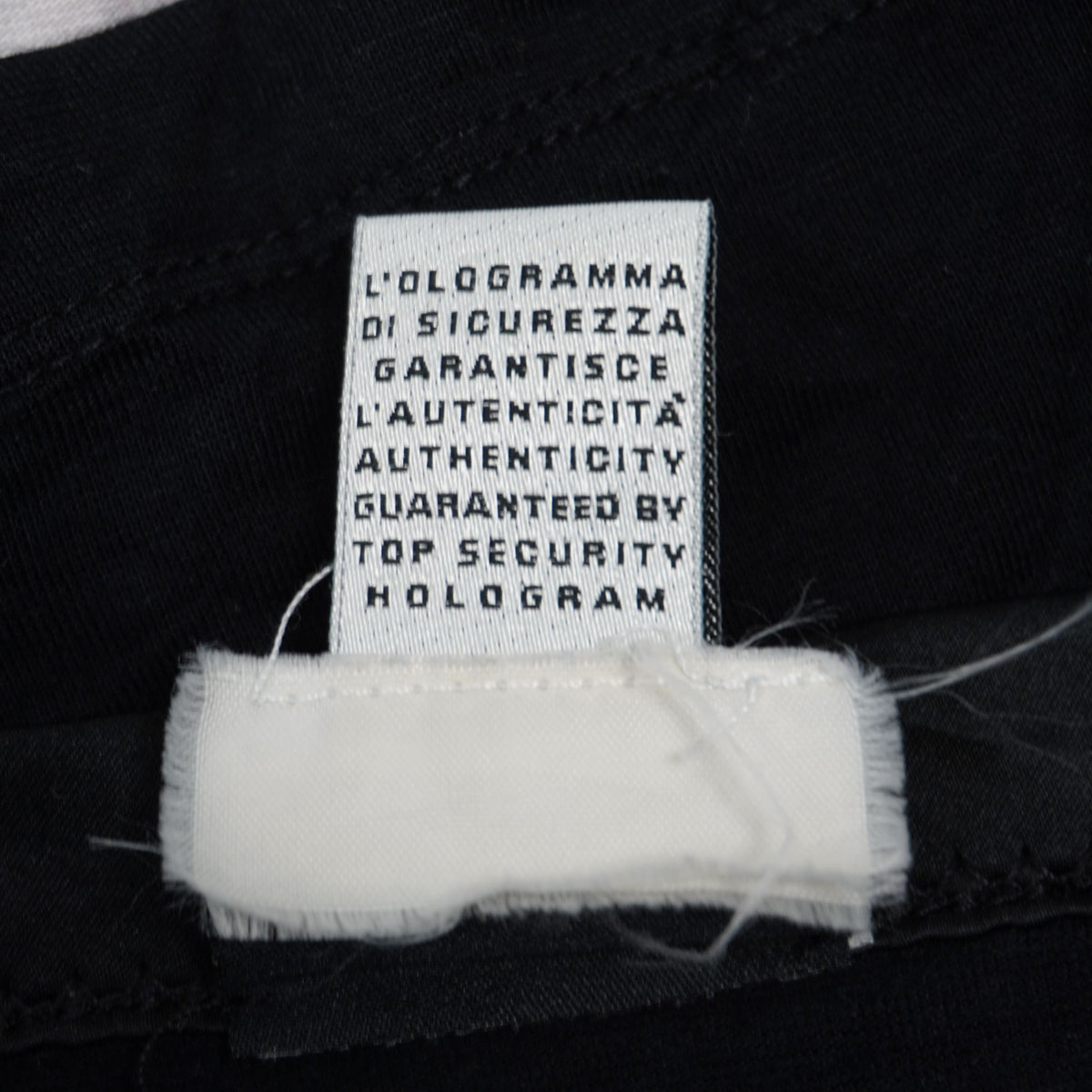 Dettaglio del cartellino interno in tessuto bianco con la dicitura sulla garanzia di autenticità tramite ologramma di sicurezza.