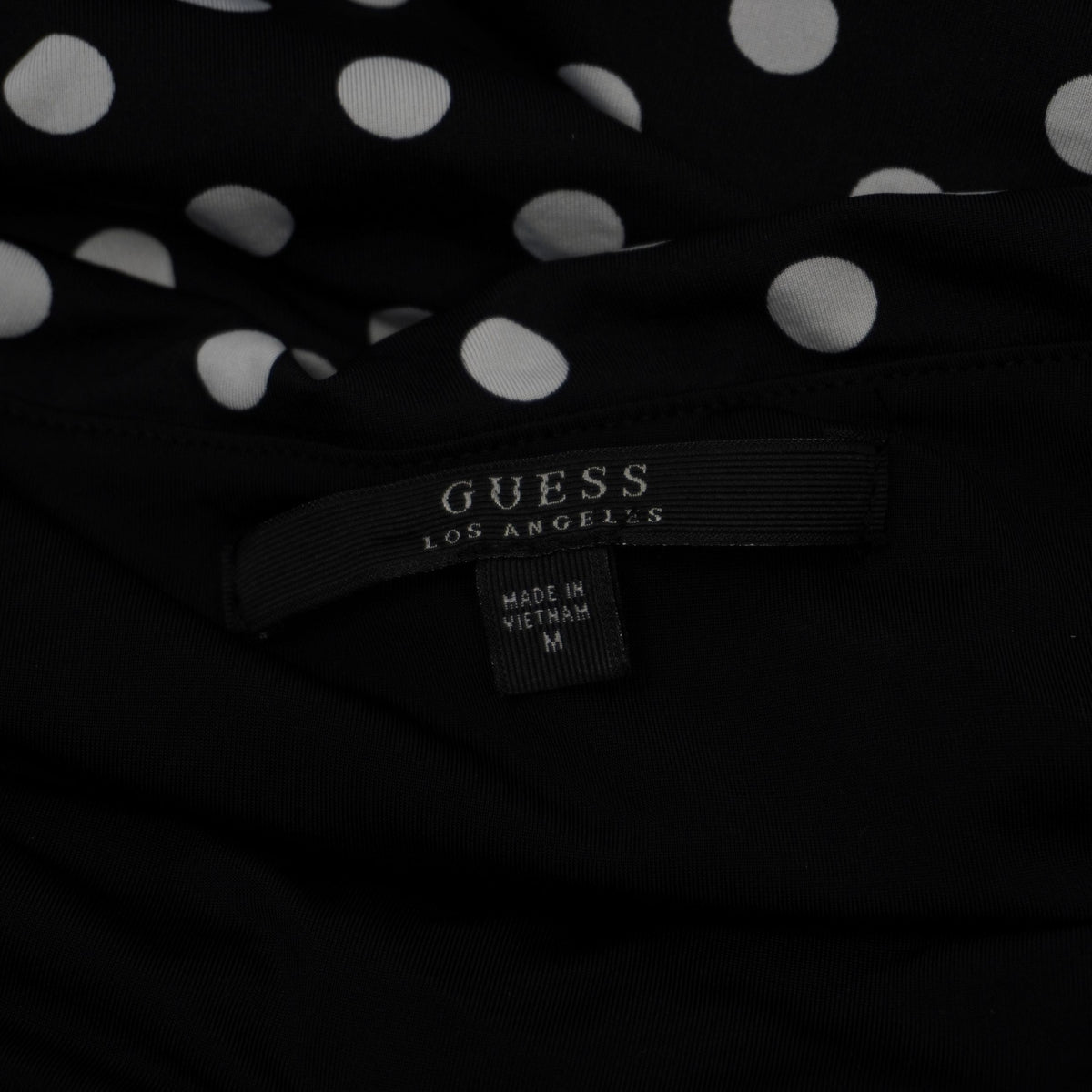 Etichetta interna in tessuto nero con logo GUESS Los Angeles e indicazione della taglia M cucita sul vestito.