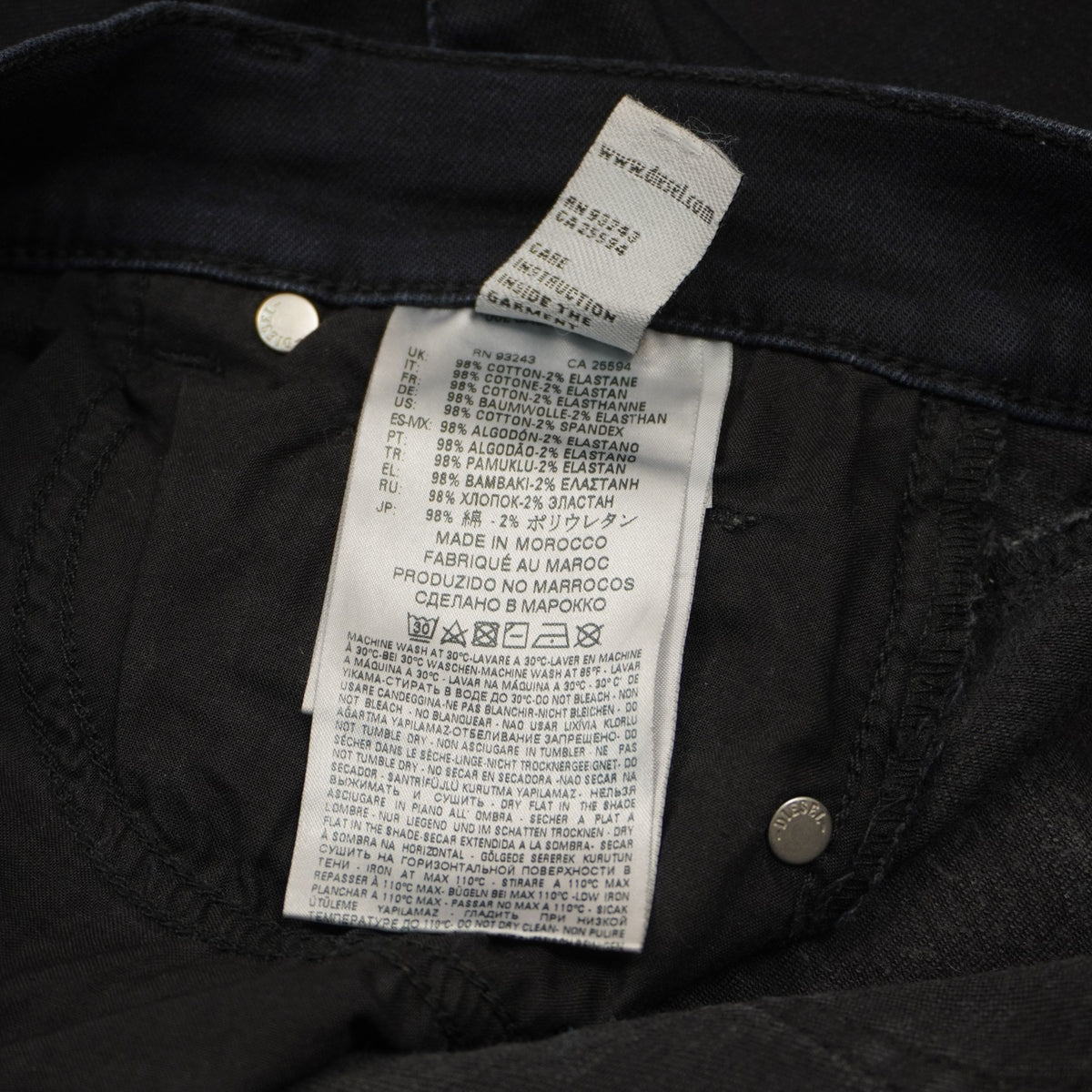 Dettaglio del cartellino interno bianco verticale con i simboli di manutenzione e lavaggio a 30 gradi del denim stretch.