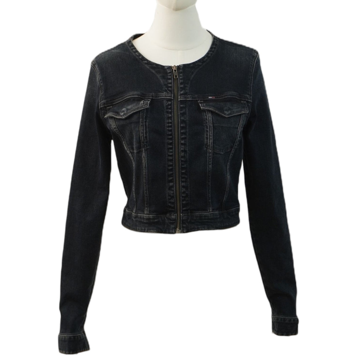 Vista frontale di una giacca di jeans corta in denim nero lavato Tommy Hilfiger su un manichino, con chiusura lampo centrale e senza colletto.
