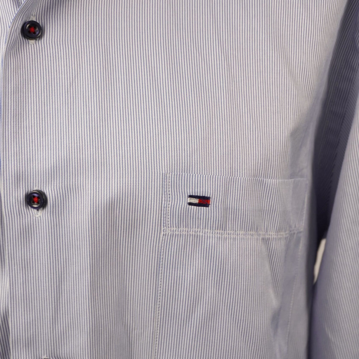 Inquadratura macro del logo a bandierina Tommy Hilfiger ricamato sul petto della camicia gessata