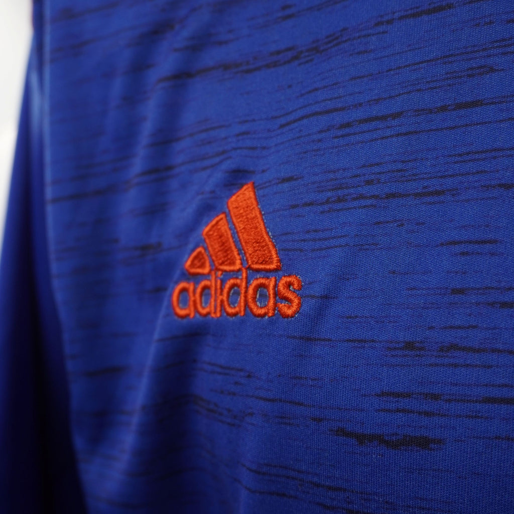 Primo piano del logo Adidas ricamato in rosso sul tessuto blu a trama melangiata.