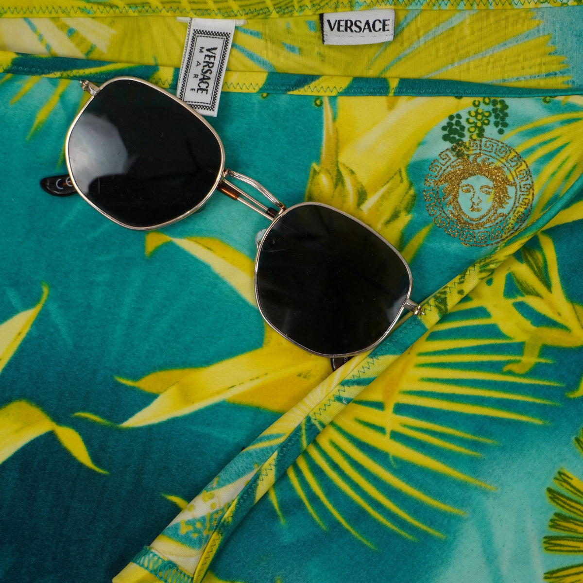  Inquadratura dall'alto del tessuto Jungle Print Versace con stemma della Medusa ricamato e occhiali da sole.